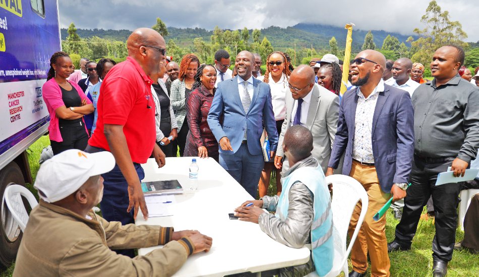 A group of people gathered outdoors at a community event, talking and laughing around a table in a field.