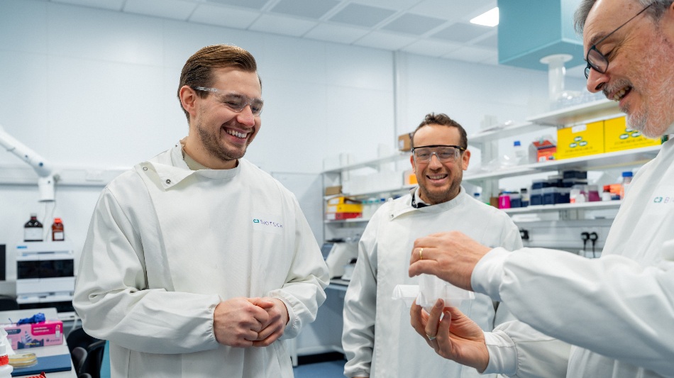 Three people in a laboratory wearing protective coats and safety glasses.