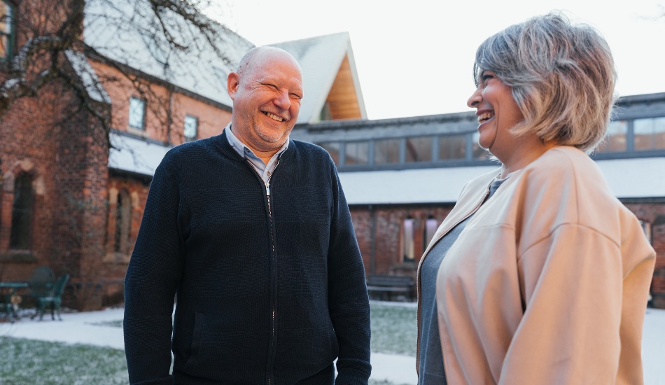 Two people standing outdoors and laughing together in a courtyard.