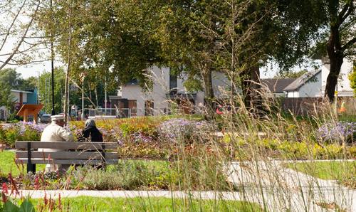 Two people sitting on a bench in a landscaped park with trees, flowers and winding paths.
