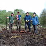 A group of people stand in a muddy field holding spades