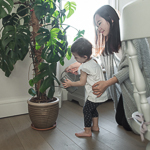 A little girl waters a big plant with help from her mum