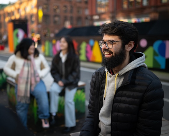 Laughing student in a Manchester street with students sat behind them.