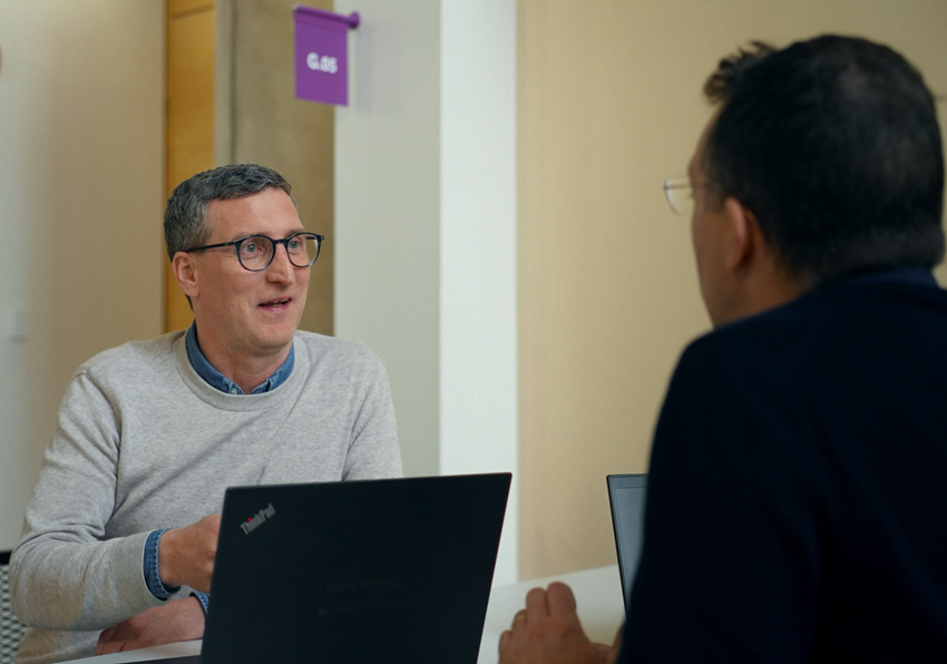 two men talking at a desk