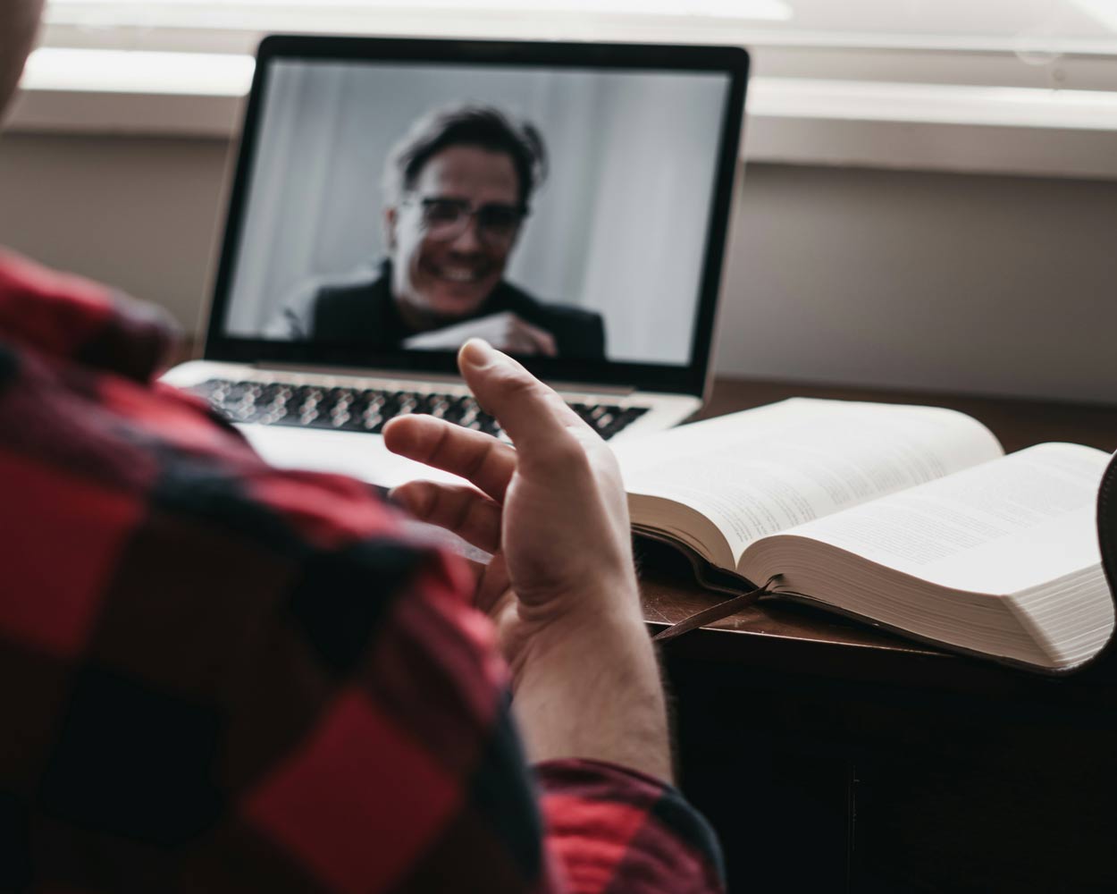 A person in an online meeting with a book on a desk