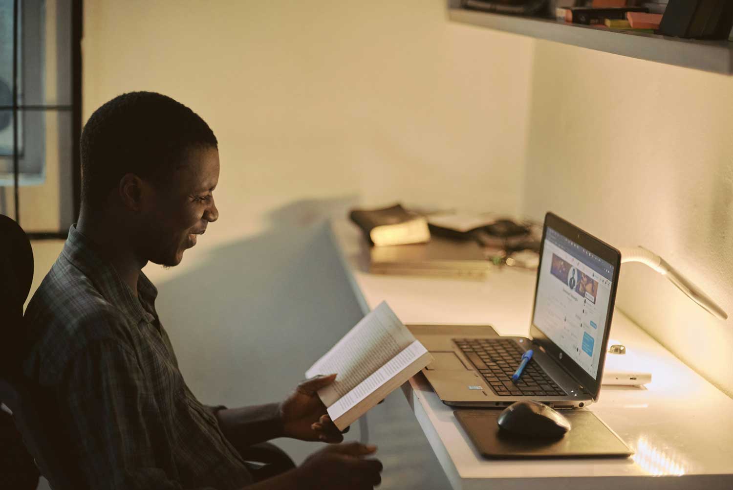 A man  reading a book at a laptop