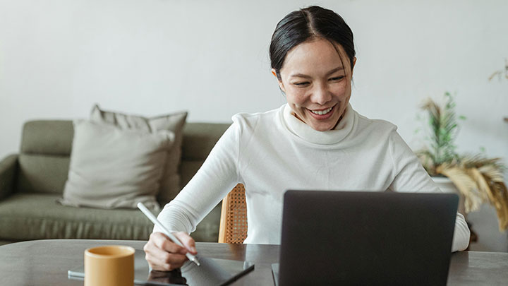 woman sat at a desk smiling at her laptop