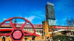 An industrial wheel statue in front of the Manchester Deansgate railway tracks and Beetham Tower. 