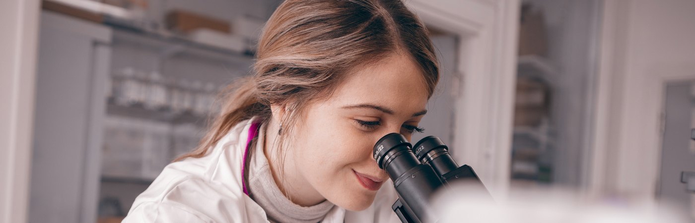Student at work in lab, looking into microscope