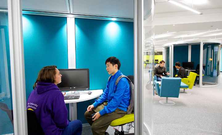 Two people talking at a desk in a glass-walled careers mentoring space.
