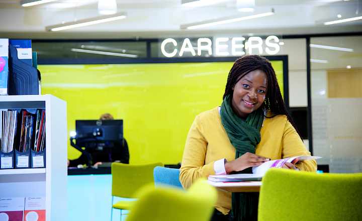 Student sitting at a table reading a booklet in a careers office, with a ‘Careers’ sign in the background.