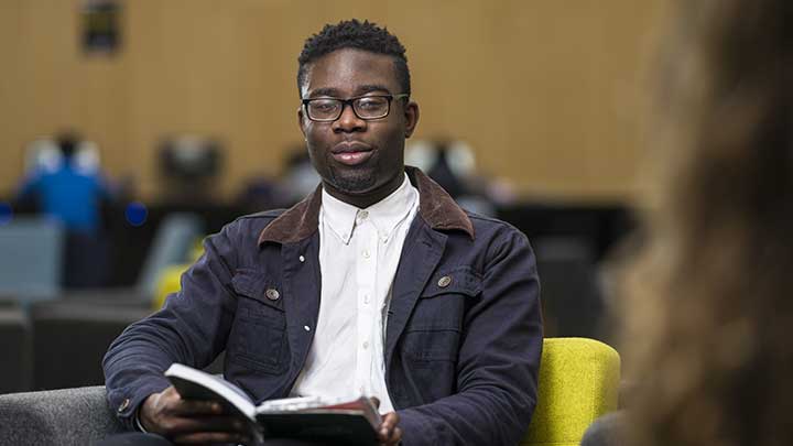 Male student sat down on chair reading in AMBS