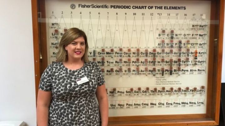 Philippa standing in front of a periodic table.