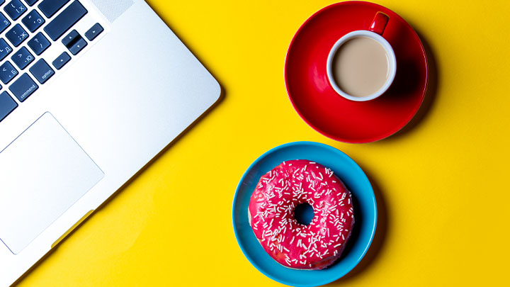 Bright desk with laptop, donut and teacup