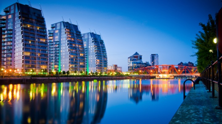 Row of tall buildings at Salford Quays reflected in water at night.