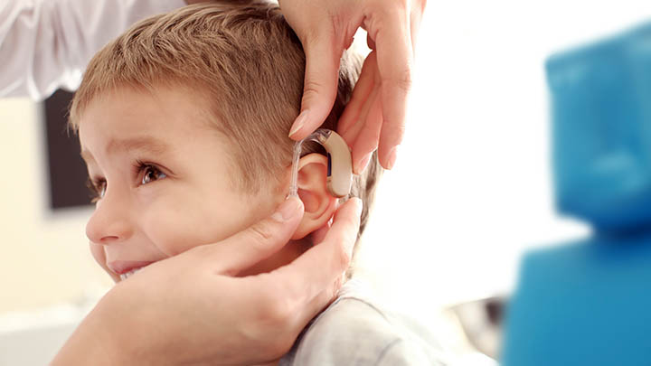Fitting a hearing aid in a boy's ear.