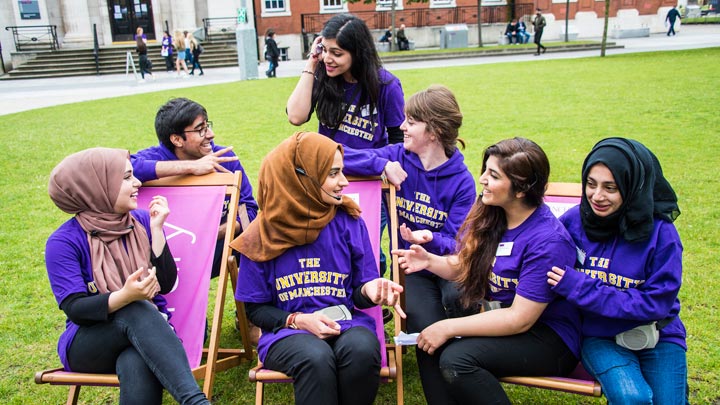 A group of students outside seated on chairs with others standing