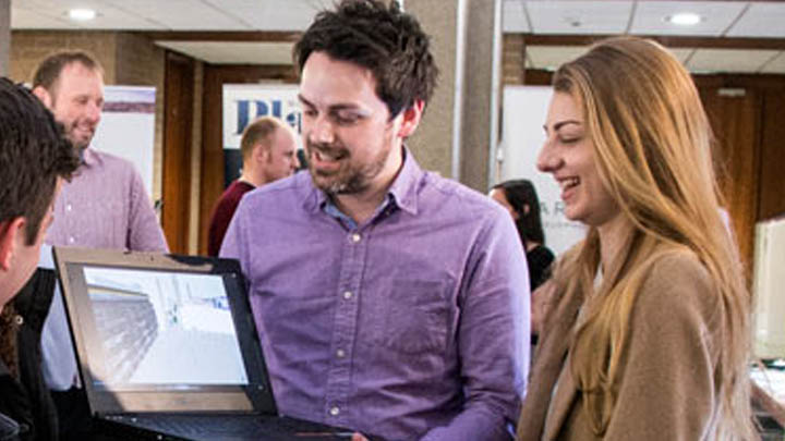 Group of students stood around a computer and smiling