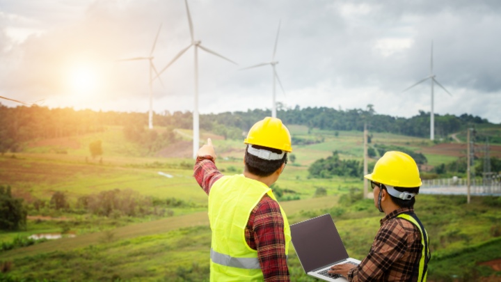 Two men in high visibility jackets in front of field of wind turbines