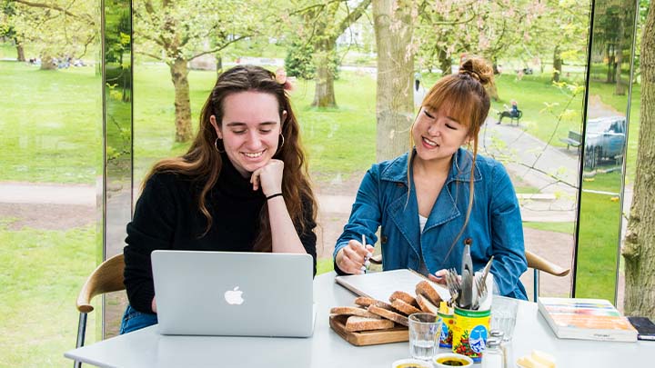 Two smiling female students looking at a laptop