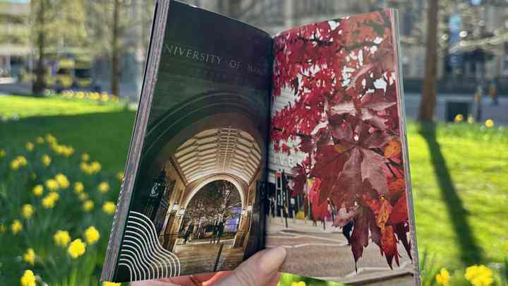A printed copy of the photobook being held open in front of the Whitworth Hall at Manchester.
