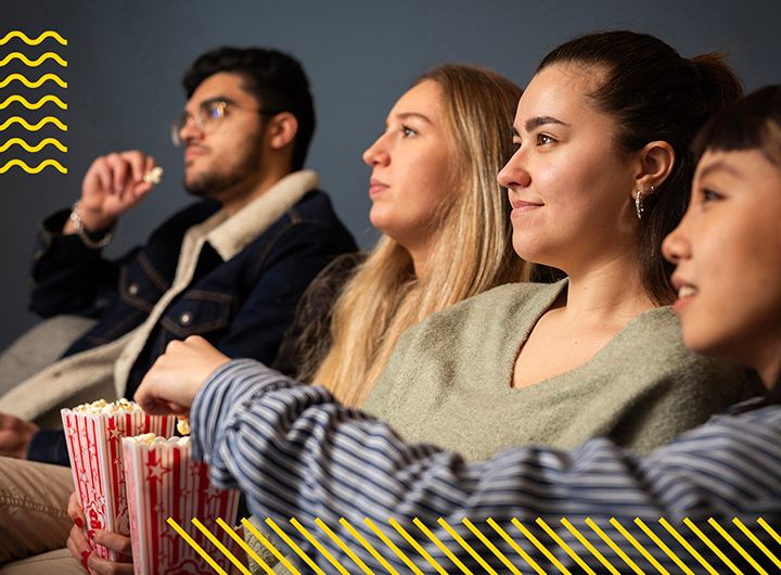 Four students eating popcorn and watching screen